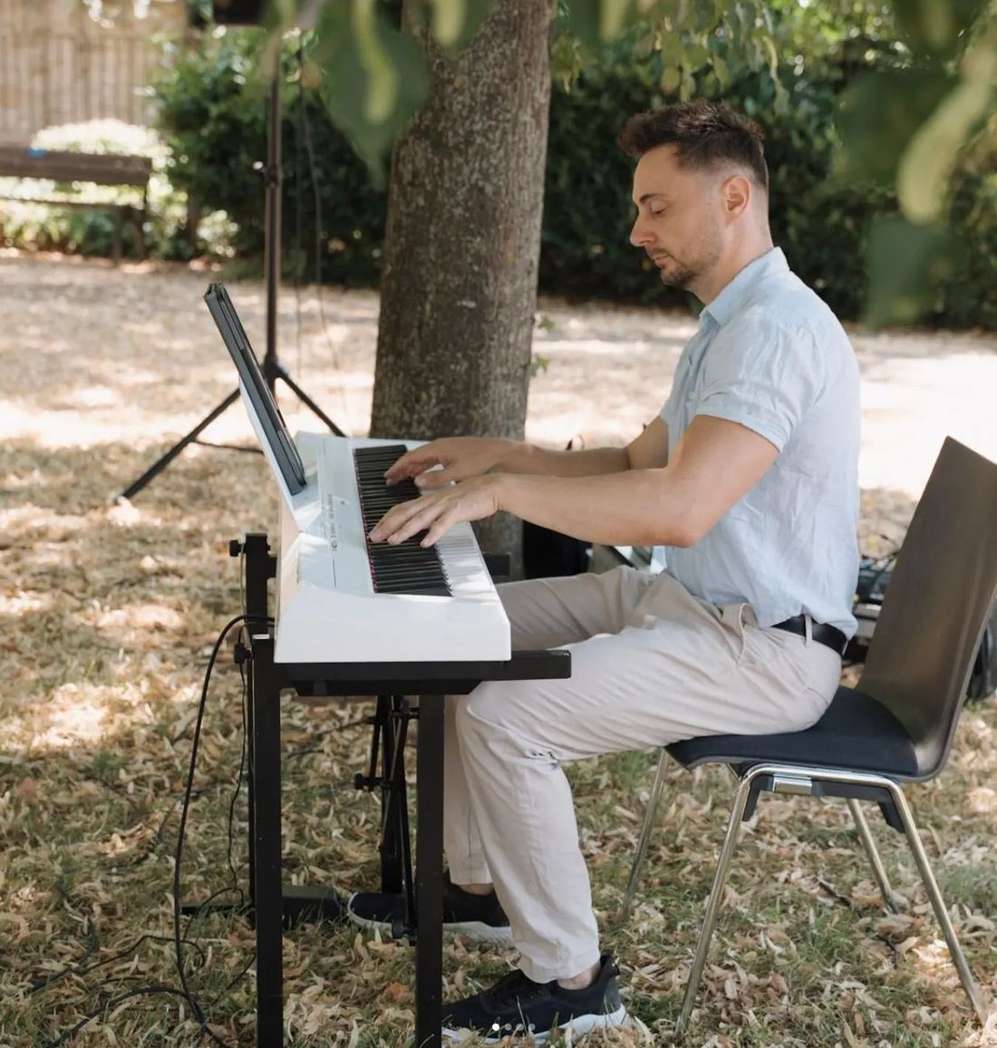 Artur Schall spielt ein weißes Digitalpiano im Schatten eines Baumes.