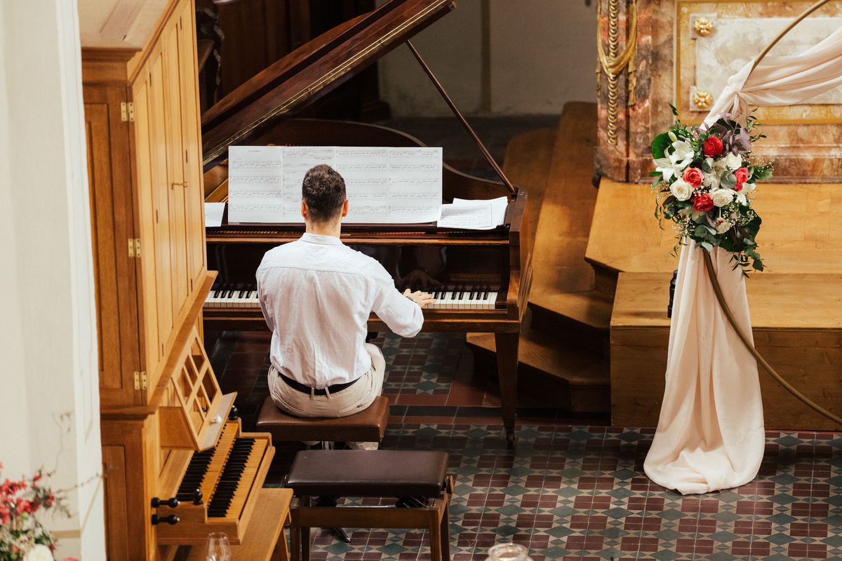 Pianist am Flügel neben weißem Blumenschmuck in einem festlichen Raum.